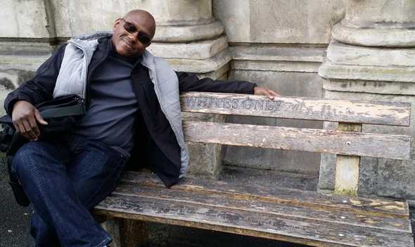 Adam sitting on a wooden bench that says "Whites Only" on it. Photo by Waheed Adams.